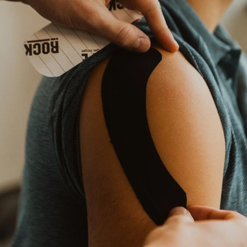 Practitioner applying black kinesiology tape along patient's shoulder and deltoid muscle in Kelowna