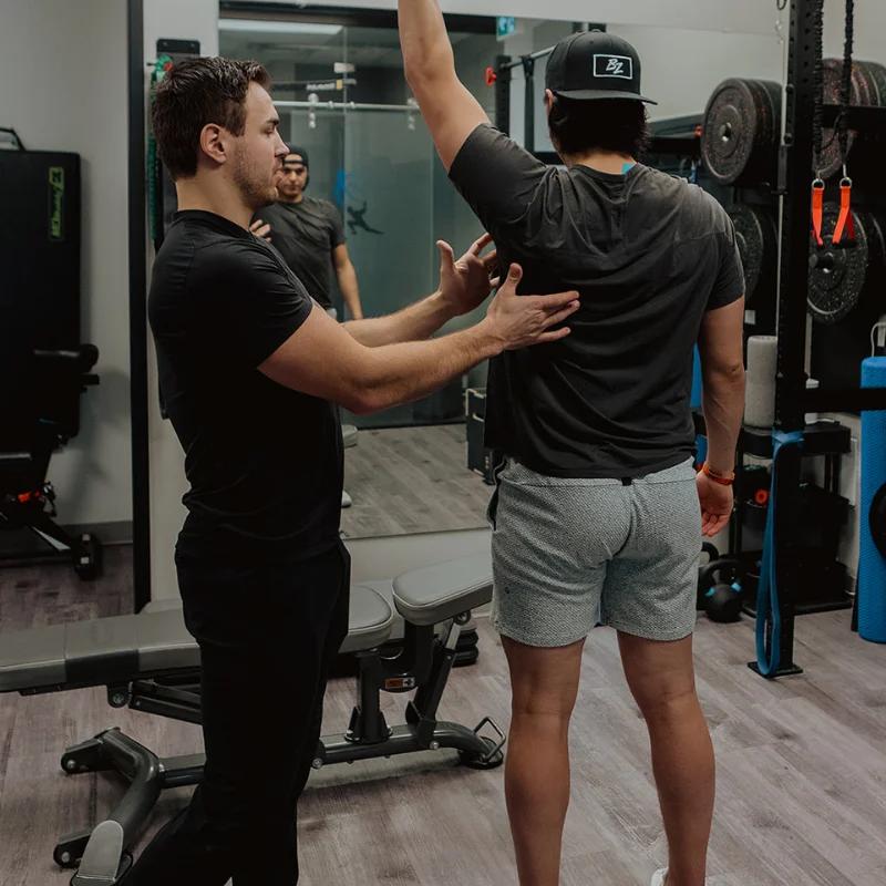 Practitioner guiding patient's overhead arm raise to assess thoracic mobility during chronic pain rehab in Kelowna