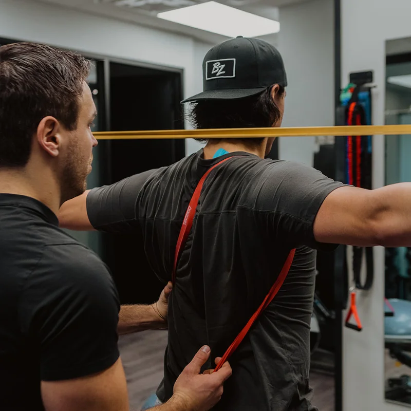 Patient performing resistance band shoulder exercise with practitioner support during chronic pain rehab in Kelowna