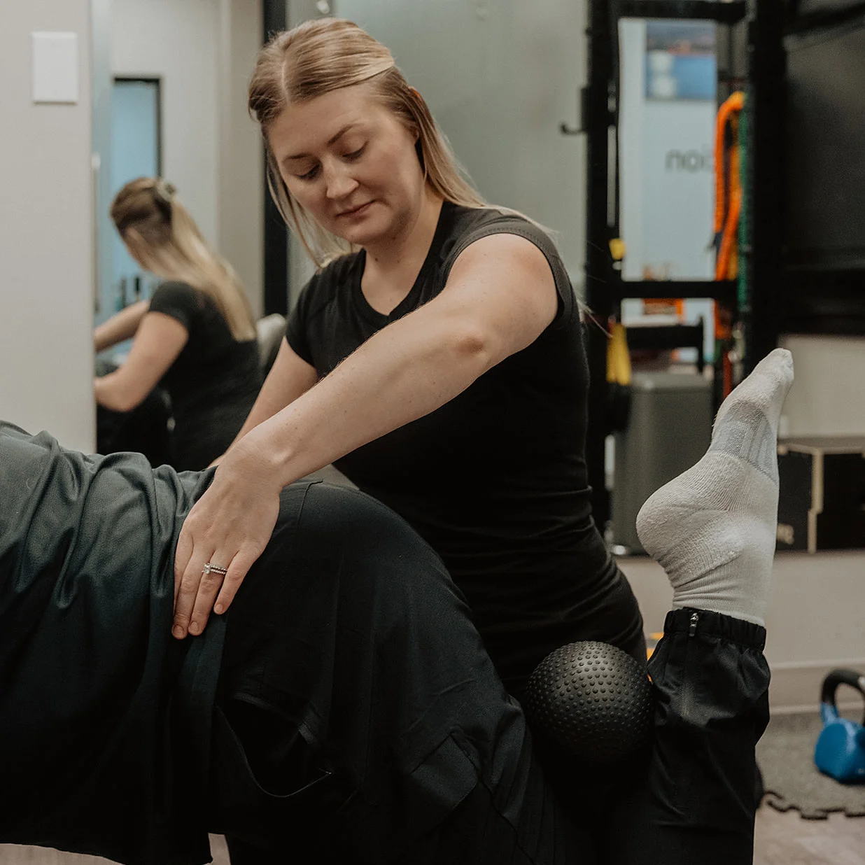 Registered massage therapist guiding patient through hip and knee alignment exercise with massage ball in Kelowna
