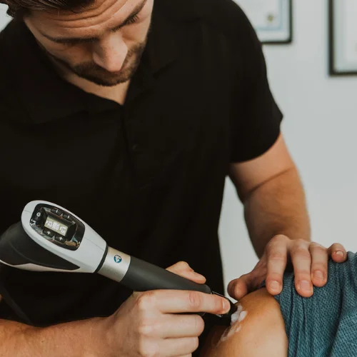 Physiotherapist applying shockwave therapy to patient's shoulder for rotator cuff and tendon pain in Kelowna