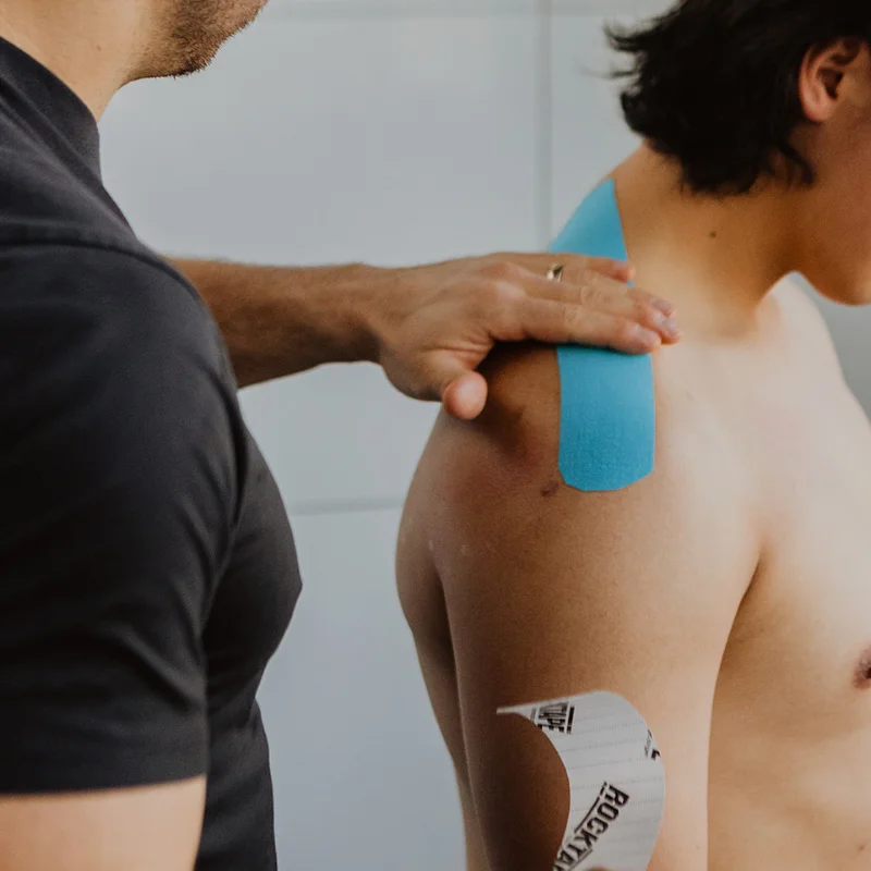 Therapist applying kinesiology tape on shoulder for stability and injury support at Pro Motion Clinic