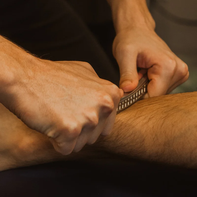 Practitioner using metal IASTM tool on patient's lower leg to break up soft tissue restrictions in Kelowna