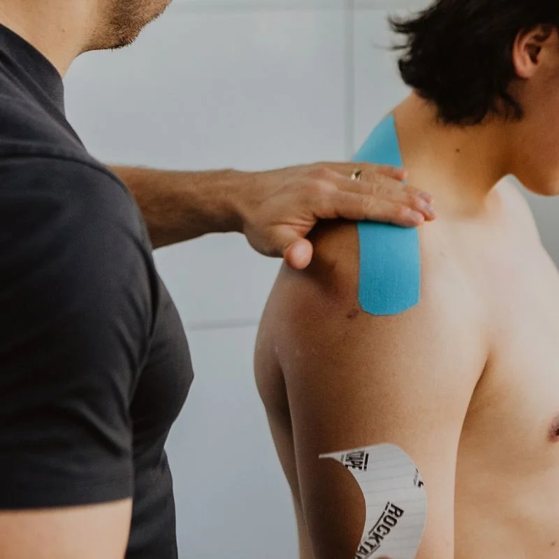 Physiotherapist applying blue kinesiology tape to patient's shoulder for support and pain relief in Kelowna