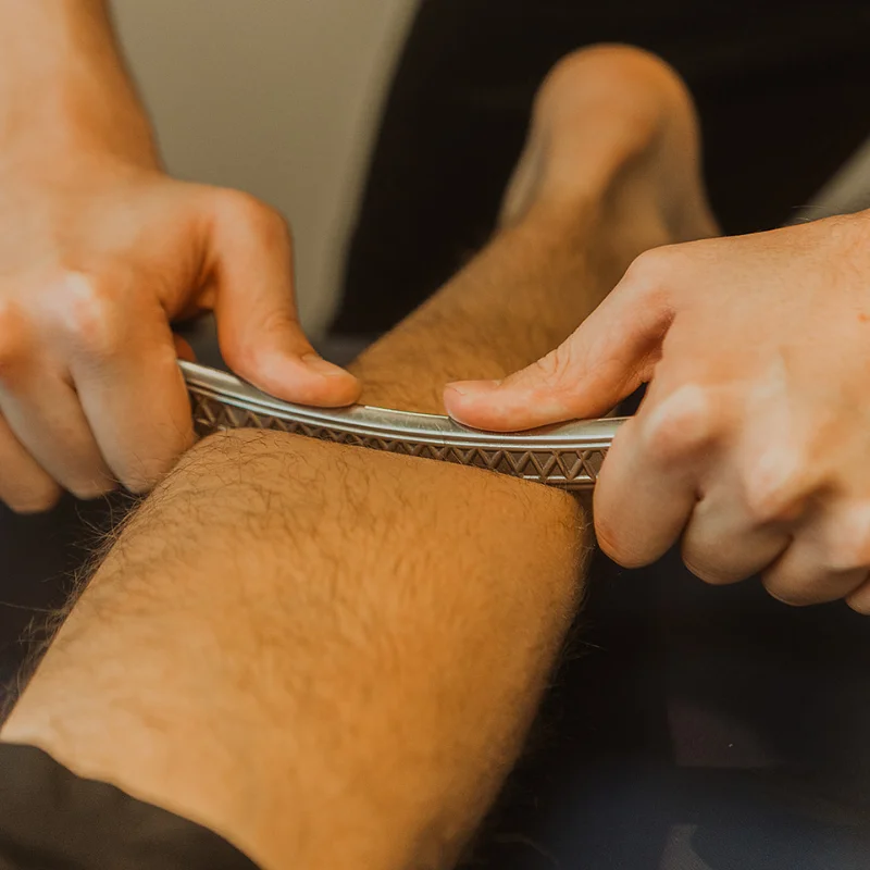 Close-up of IASTM metal tool applied to patient's knee and thigh to release soft tissue adhesions in Kelowna