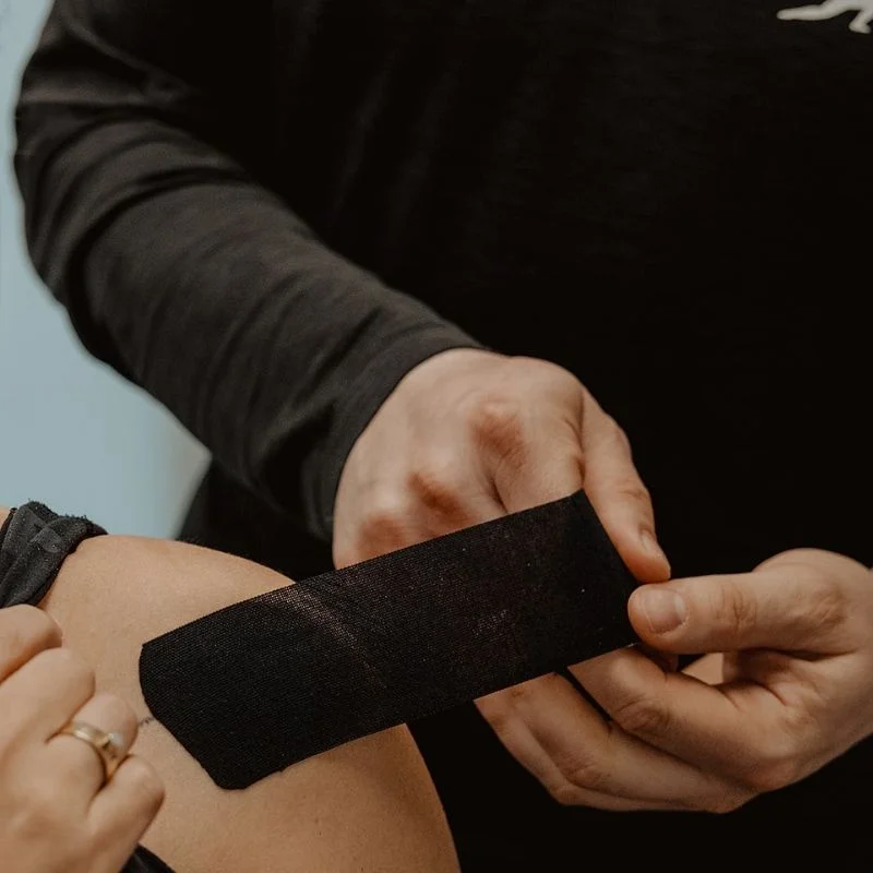 Physiotherapist applying rigid athletic tape to patient's knee for joint support during injury recovery in Kelowna