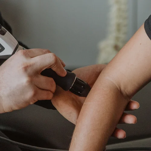 Practitioner applying shockwave therapy to patient's elbow for tennis elbow and tendon pain treatment in Kelowna