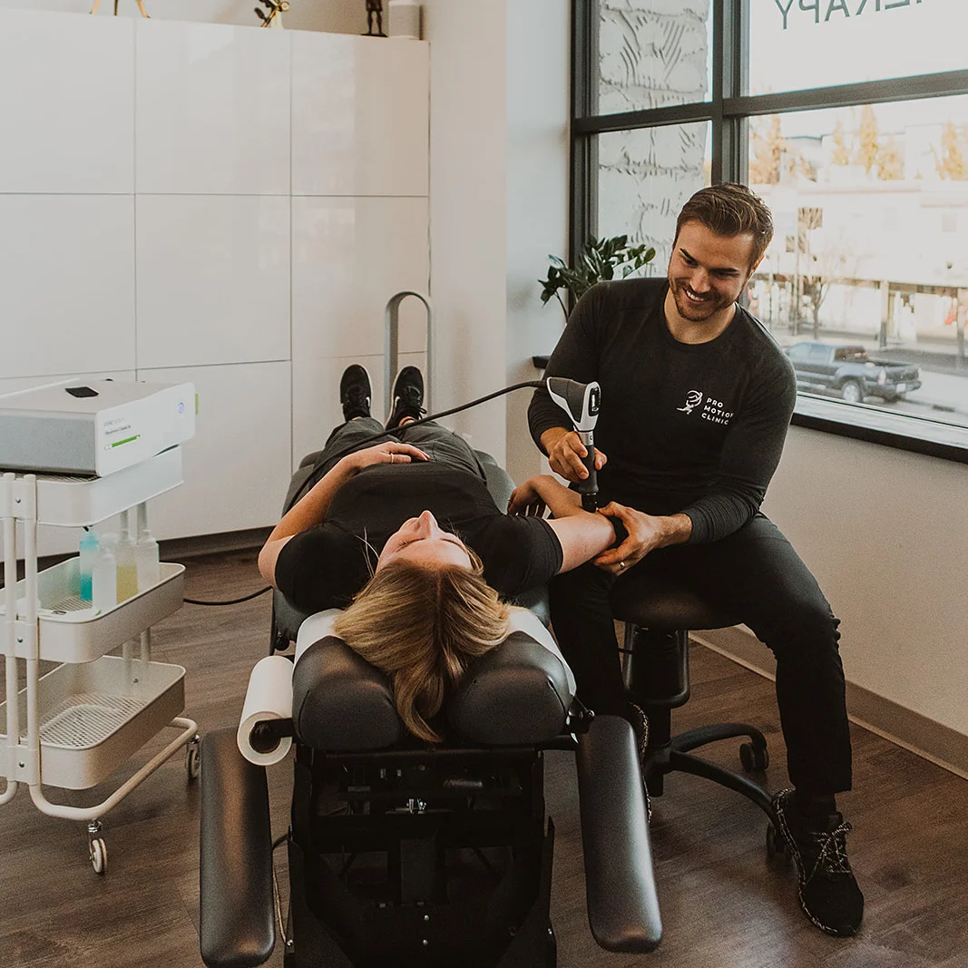 Pro Motion Clinic physiotherapist applying shockwave therapy to patient's knee in Kelowna treatment room