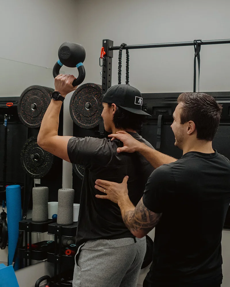 Kinesiologist supervising overhead kettlebell exercise for shoulder strength at Pro Motion Clinic