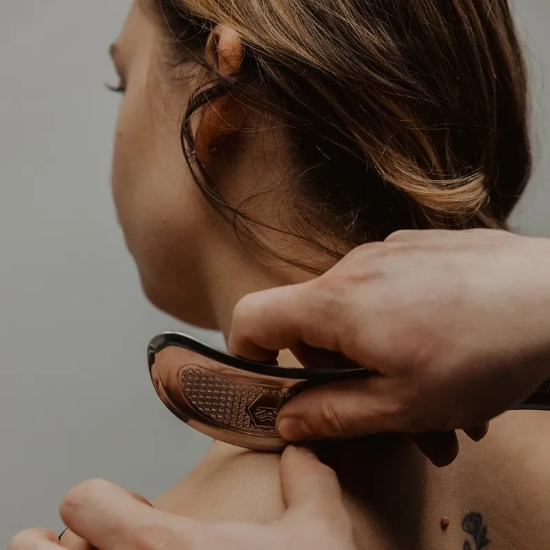 Practitioner applying IASTM tool to patient's neck and upper trapezius for soft tissue mobilization in Kelowna
