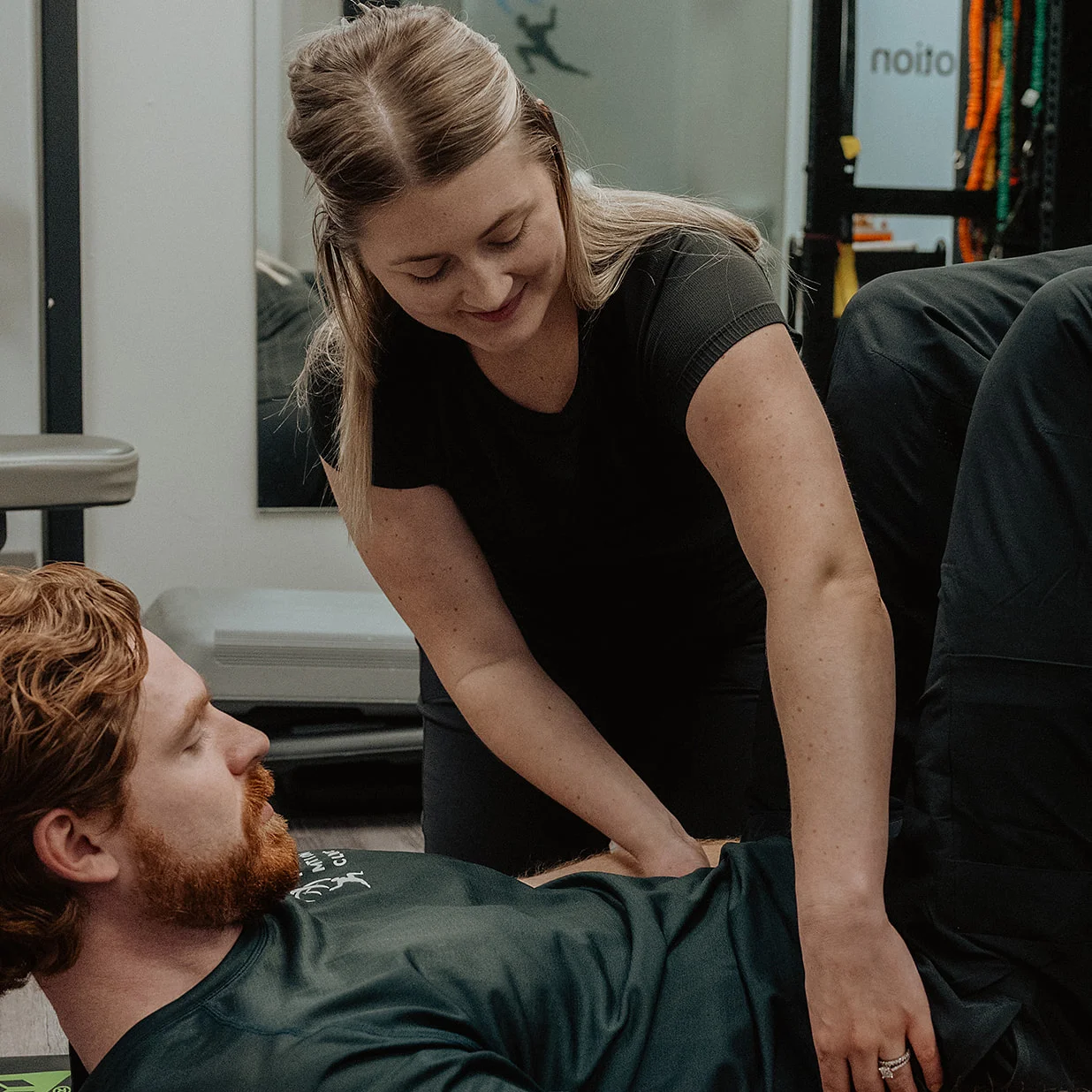 Registered massage therapist supporting patient's lower back during clinical Pilates exercise in Kelowna clinic