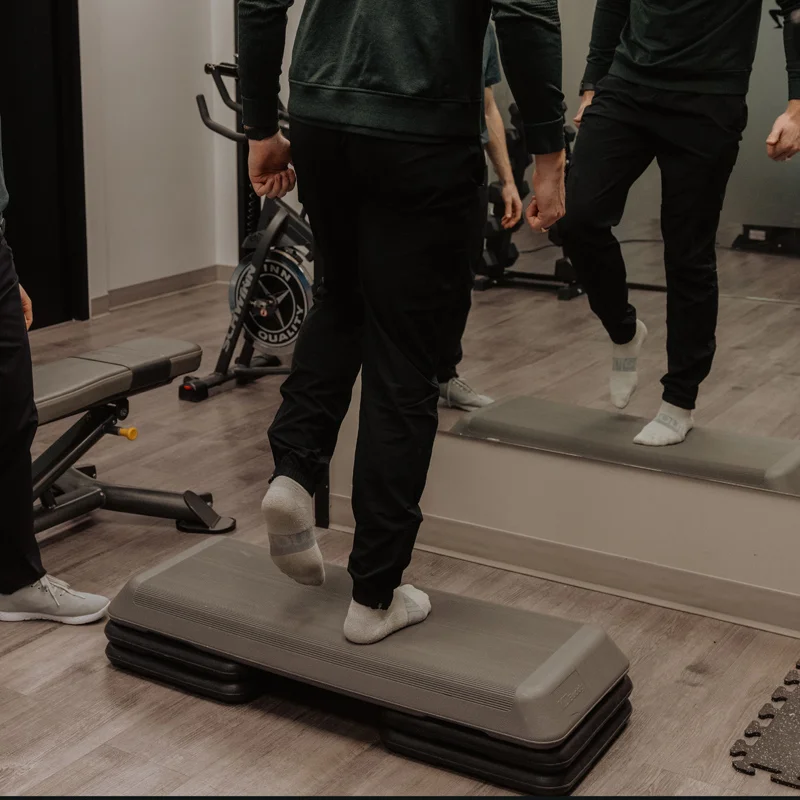 Patient performing step-up exercise on platform during post-surgical lower limb rehabilitation in Kelowna clinic