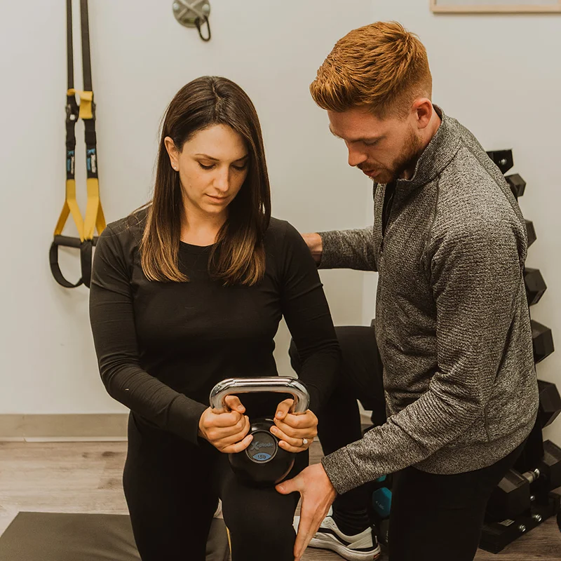 Physiotherapist coaching female patient through kettlebell exercise during post-surgical rehabilitation in Kelowna