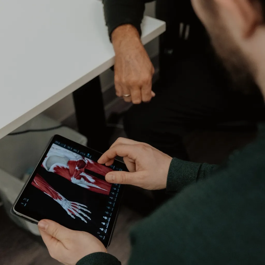 Chiropractor explaining forearm and muscle anatomy on tablet during Veterans Affairs medical questionnaire assessment in Kelowna