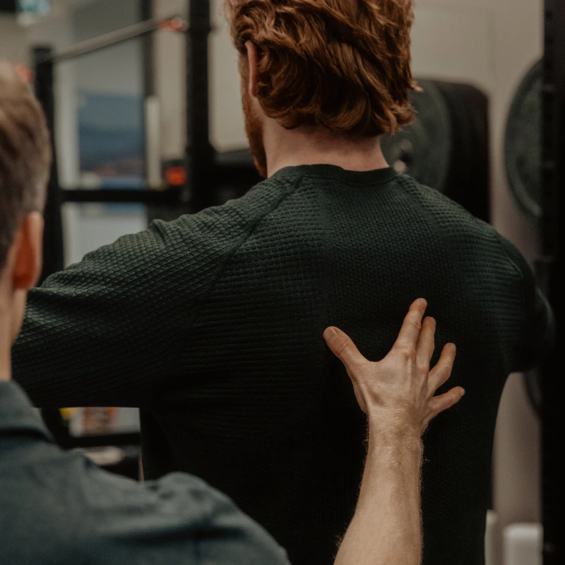 Chiropractor palpating patient's lower back during TPI golf fitness assessment in Kelowna