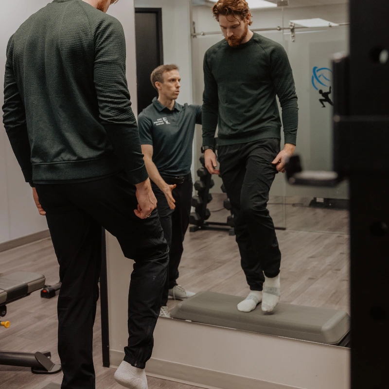 Chiropractor observing patient performing single-leg balance movement screen for TPI assessment in Kelowna