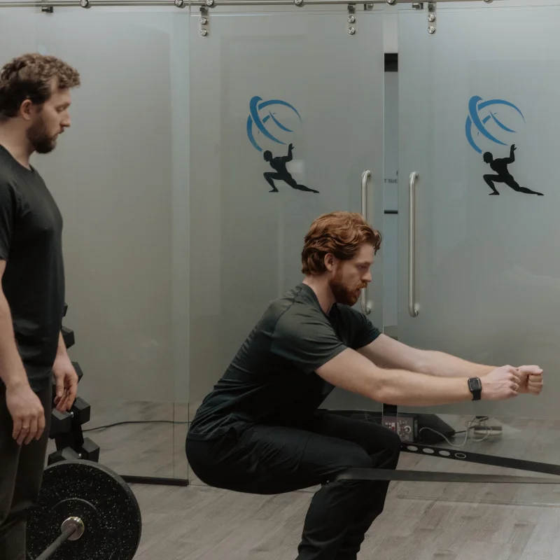 Practitioner assessing patient's squat mechanics during chronic pain rehabilitation session in Kelowna clinic