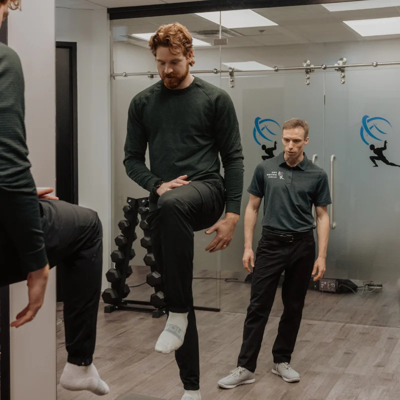 Pro Motion Clinic practitioner supervising single-leg balance exercise for chronic pain and movement rehabilitation in Kelowna