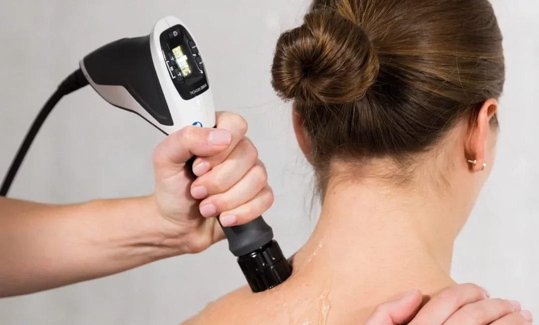 Practitioner using a shockwave therapy device on a patient’s upper back and neck